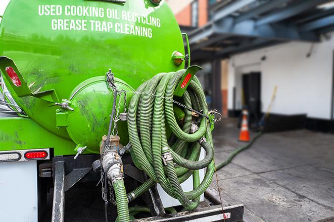 a professional plumber using a pump to empty a grease trap in Babson Park MA